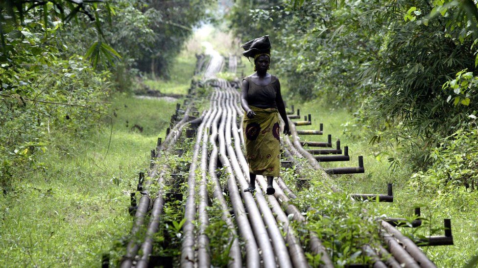 A woman walks along an oil pipeline in Warri, Nigeria