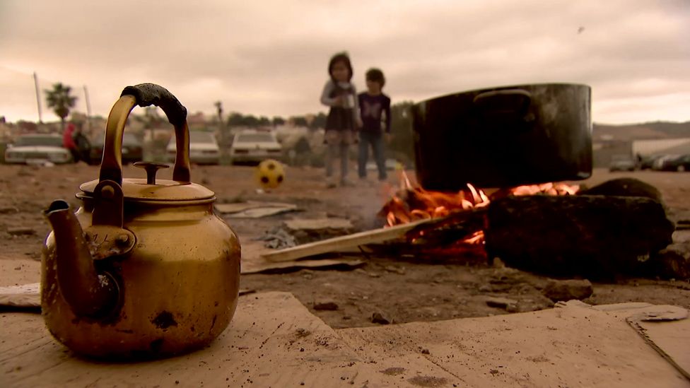 Kettle and camp fire, children in the background playing with a ball