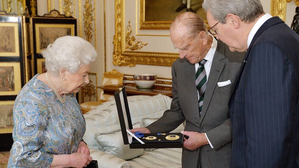 Queen Elizabeth II talks with the Australian High Commissioner, Alexander Downer (right) as she prepares to present the Duke of Edinburgh, with the Insignia of a Knight of the Order of Australia