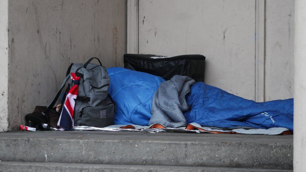 A person sleeping rough in a doorway. They are under a blue sleeping blanket.