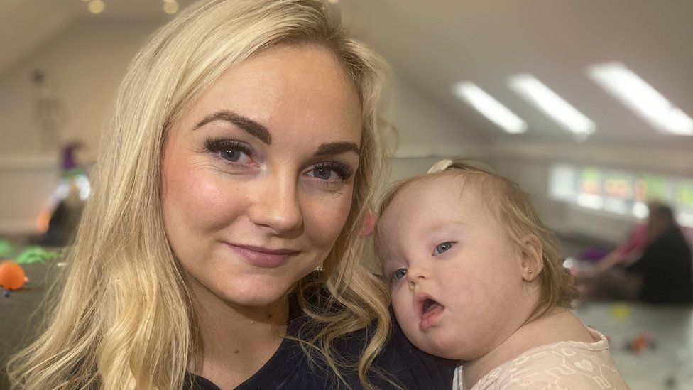 Young woman with long blonde hair holds a young child with Down's syndrome