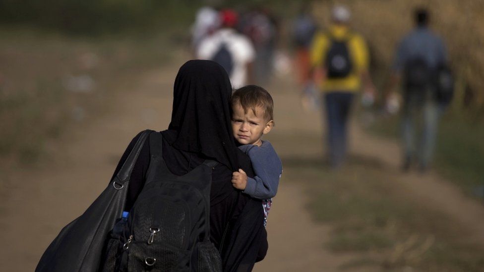 A migrant carries a child as she walks on a dirt road close to the Croatian border near the town of Sid, Serbia, September 19, 2015