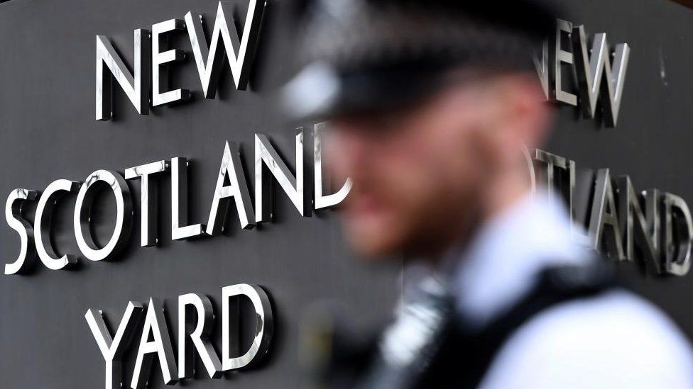 The blurred profile of a police officer in front of a New Scotland Yard sign