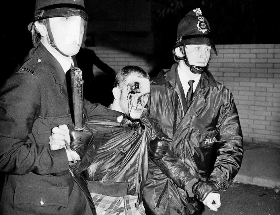 Two policemen drag a man with a bloodied face during the riots