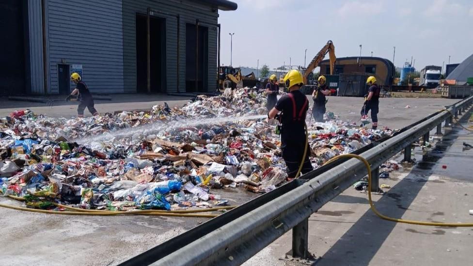 Firefighters dampen down piles of smouldering waste.