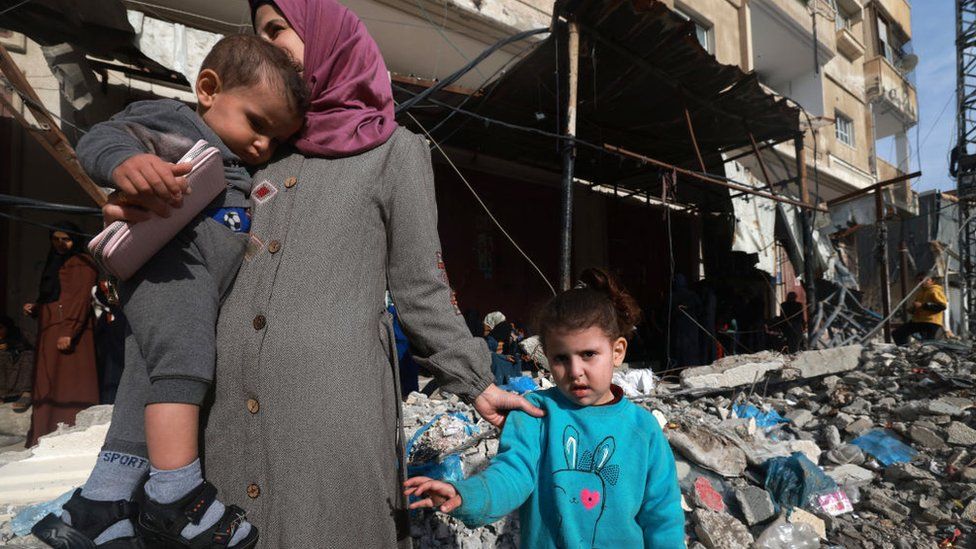 Members of a displaced Palestinian family stand amid the rubble in Rafah on a street in the southern Gaza Strip on 10 December 2023