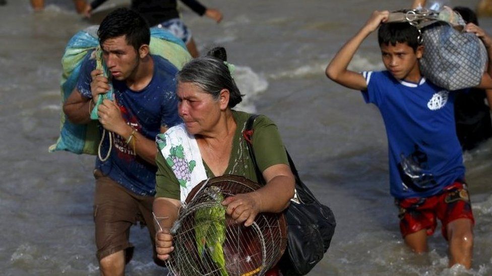 A woman carries her parrot in a cage next to people carrying their belongings to Colombia through the Tachira river on 25 August, 2015.