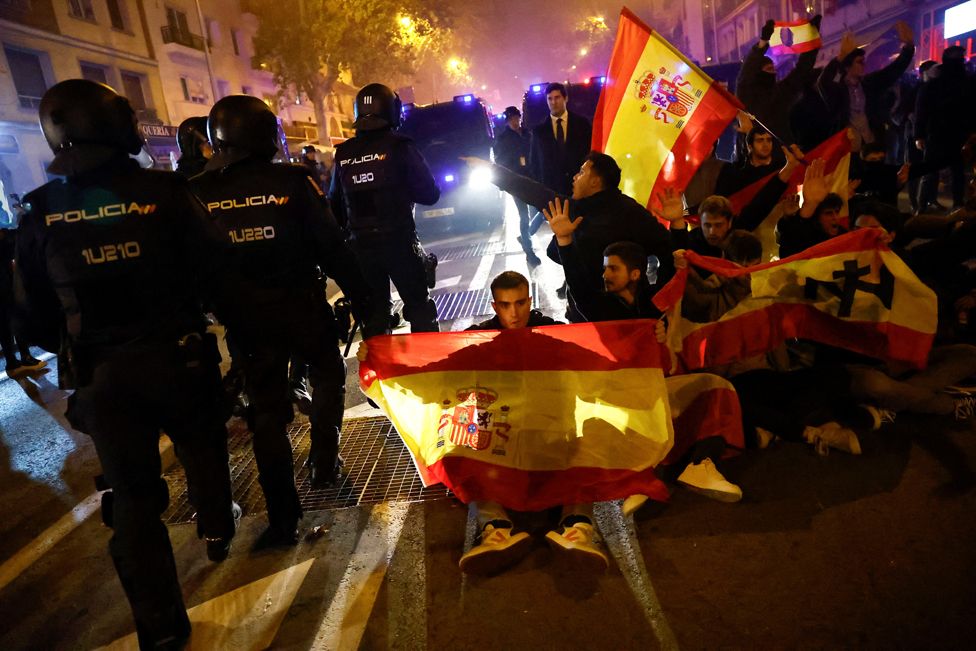 Riot police officers stand guard, as demonstrators throw smoke bombs, during a protest near Spain's Socialist Party (PSOE) headquarters in Madrid, Spain. November 16, 2023.