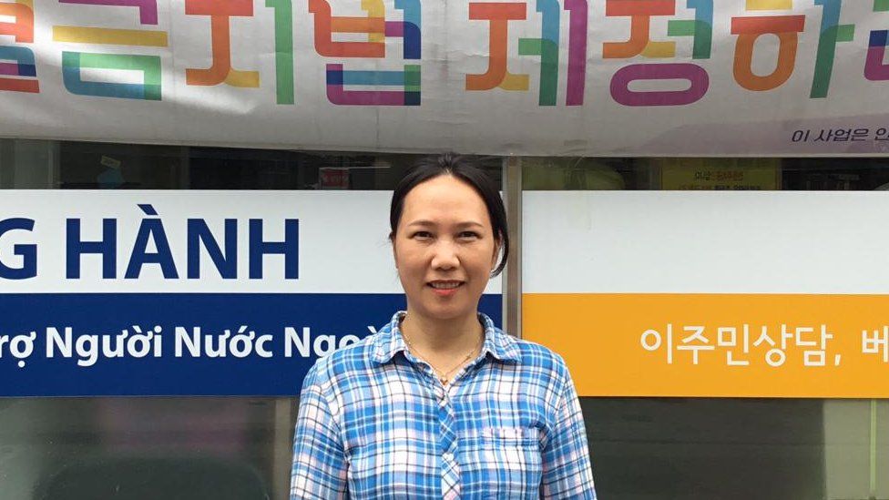 Вон Ок Кум стоит возле своего офиса с вывесками на корейском и вьетнамском языках.