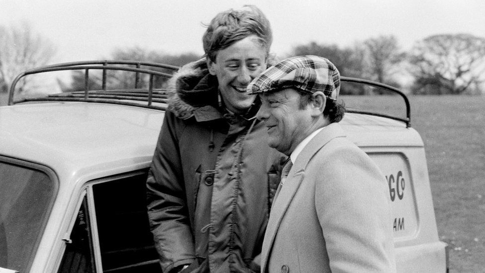 Black and white image of Nicholas Lyndhurst and David Jason laughing next to a van