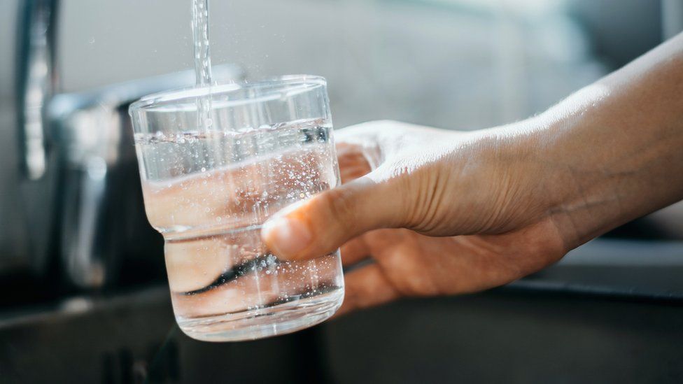 A hand holds a clear glass cup under a tap of running water