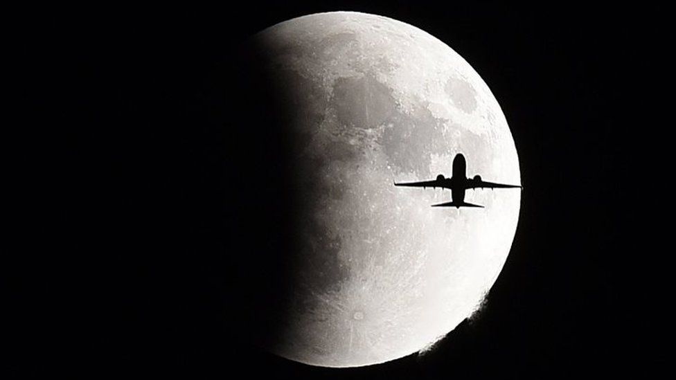 A plane flies in front of the supermoon over Geneva, Switzerland