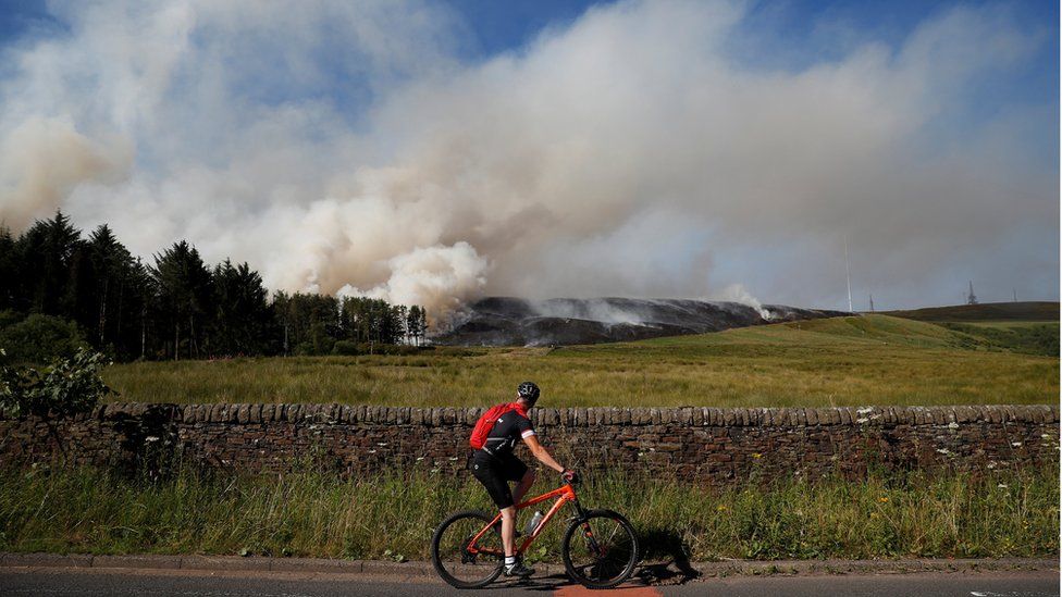 A cyclist looks at smoke rising from a moorland fire at Winter Hill, near Rivington, Britain.