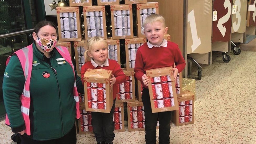 Children with supermarket worker and Christmas crackers