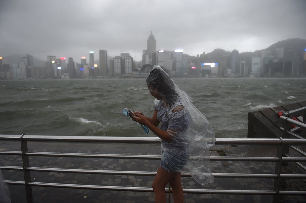 A woman uses her phone while wearing a plastic poncho along Victoria Harbour during heavy winds and rain brought on by Typhoon Hato in Hong Kong on 23 August 2017.