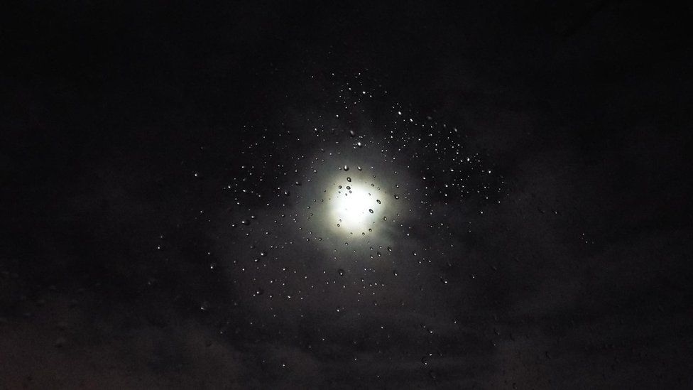 Moon seen through drops of water on a window pane