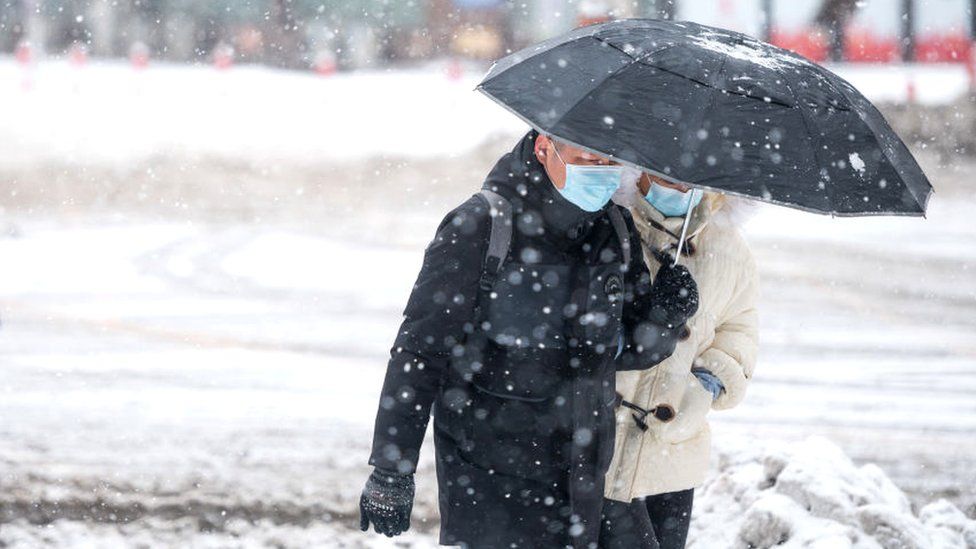 Pedestrians holding an umbrella walk along a road during a heavy snowfall on November 8, 2021