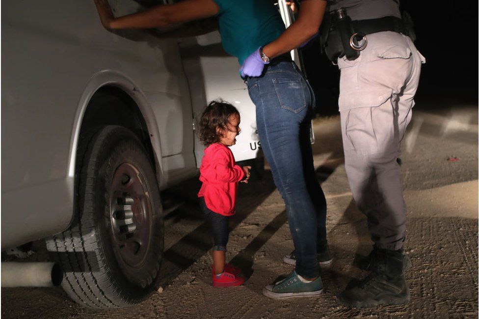 A two-year-old girl cries as her mother is searched and detained against a vehicle near the U.S.-Mexico border.
