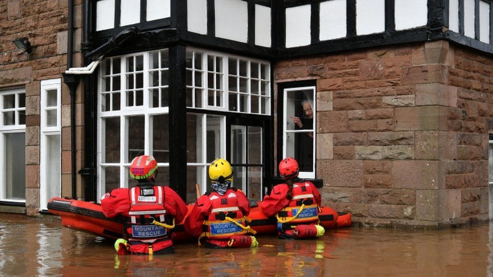 Rescuers up to their waist in floodwater outside a house