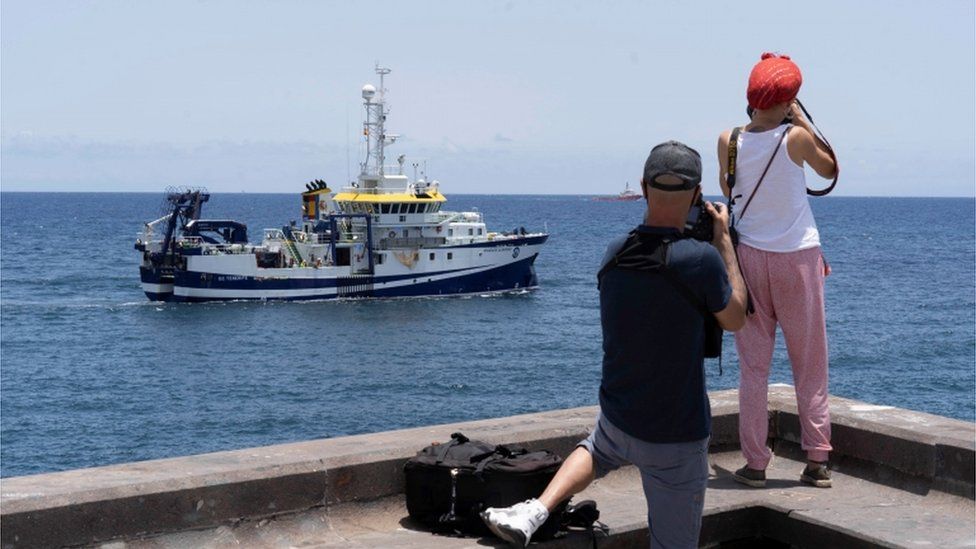 The oceanographic vessel Angeles Alvarino with two people taking a photo of it on the shore