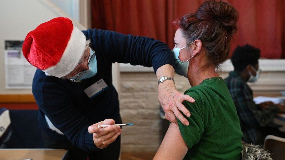 Woman receiving Covid vaccination at centre in Sheffield from medic wearing a Santa hat