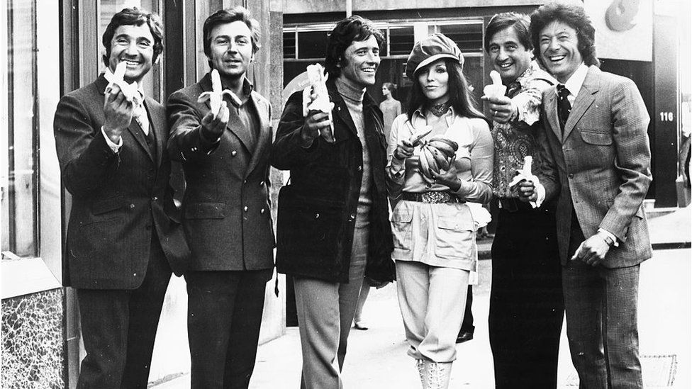 Portrait of British entertainers taking part in Mike and Bernie Winters Thames Television Spectacular holding bunches of bananas; (L-R) Mike Winters, Des O'Connor, Sacha Distel, Joan Collins, Bernie Winters and Lionel Blair, the Strand, London, September 22nd 1970. (Photo by Frank Barratt/Keystone/Getty Images)