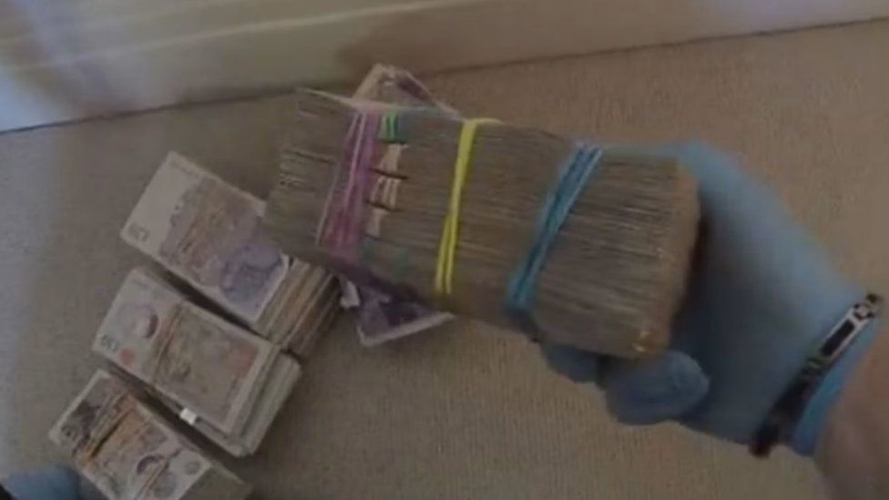 Bundles of cash in rubber bands being held by police wearing a blue rubber glove