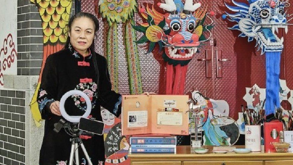 A woman stands in front of a wooden worktable surrounded an array of tools to create and design kites