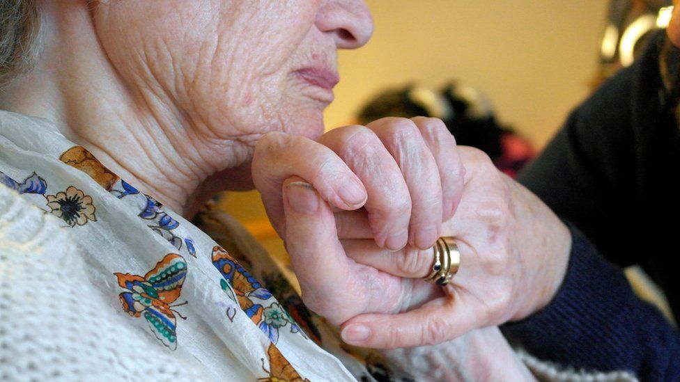 Woman with dementia holds hands with carer