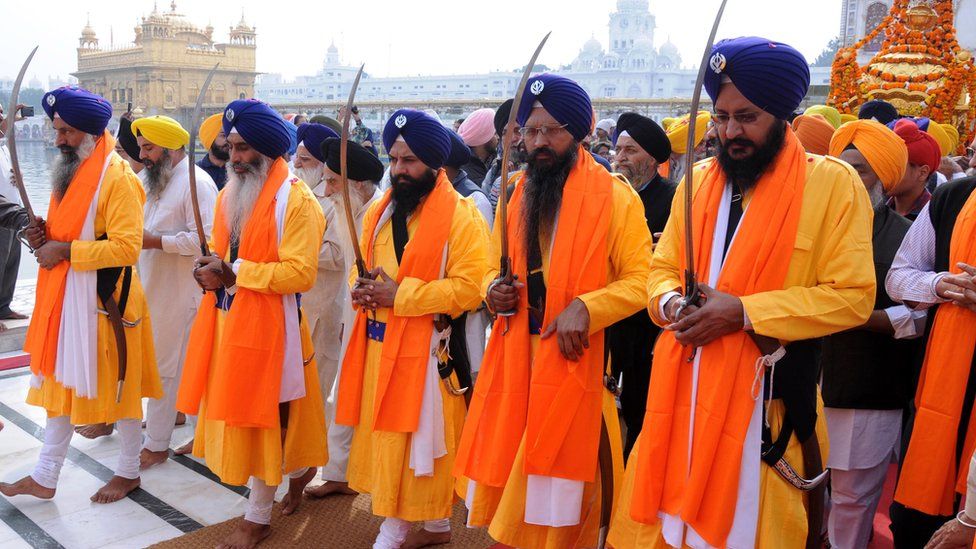 Five Beloved Ones, wearing orange robes and purple turbans and holding swords, lead a procession through the Golden Temple in Amritsar, India