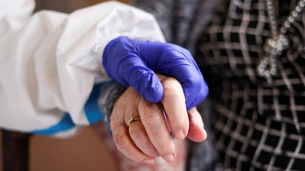 An elderly woman's hand holding a fully-gloved hand