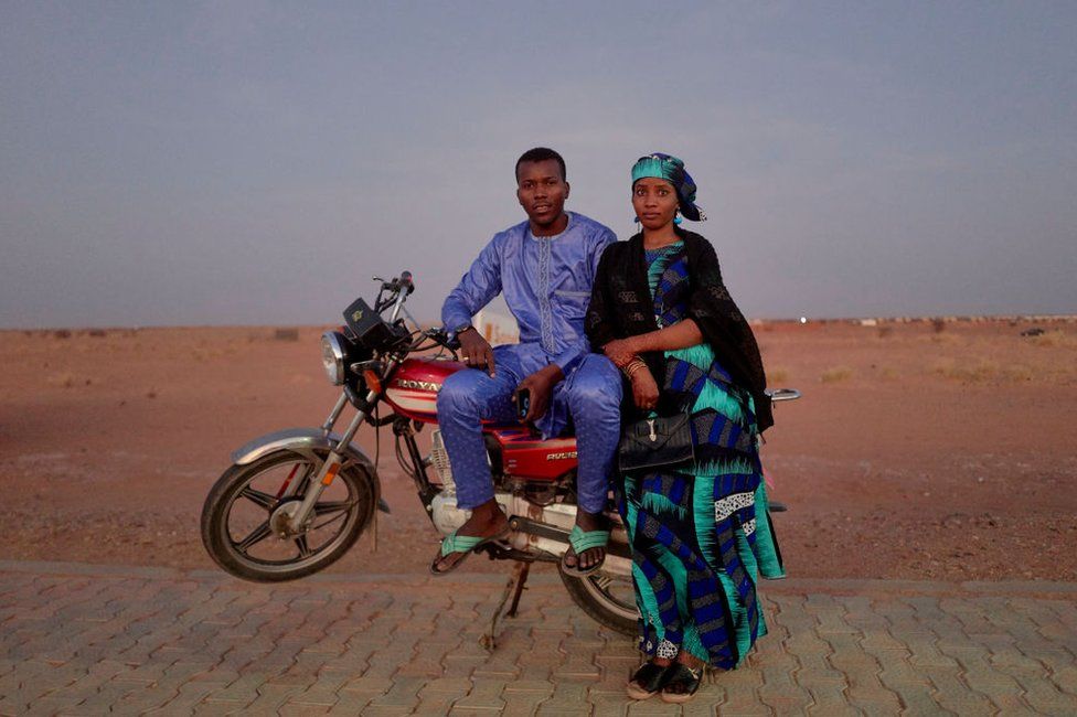 A young couple poses for a portrait on a motorbike in the desert.