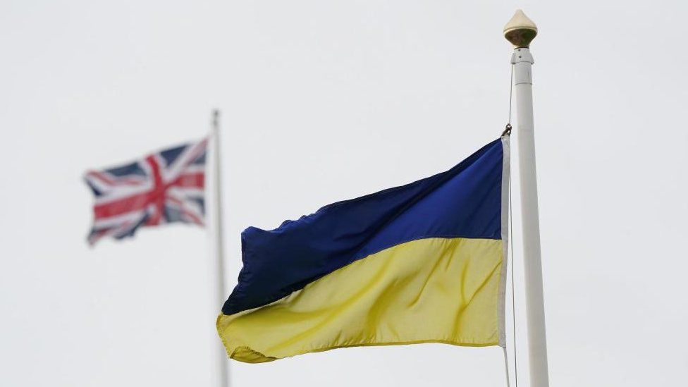 A Ukrainian flag is seen flying with a Union Jack in the background