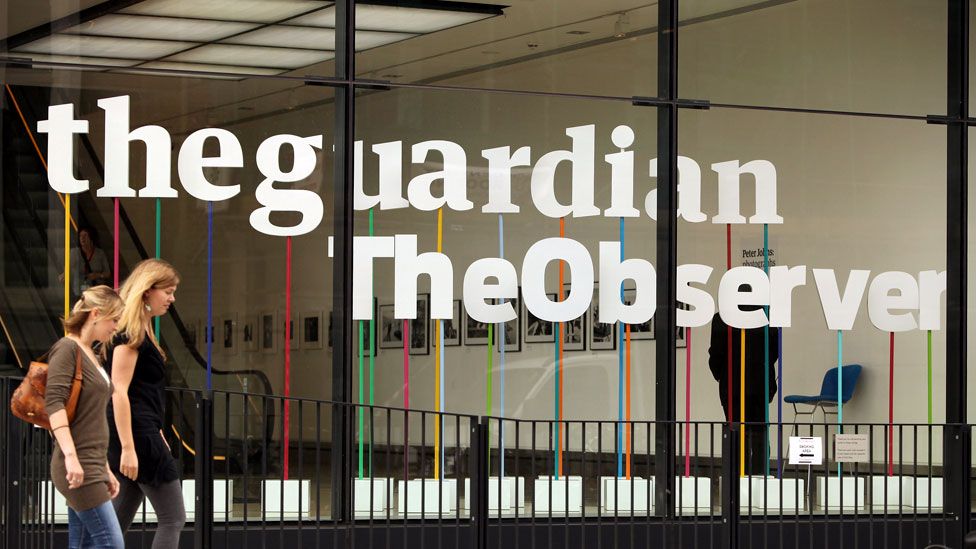 Two women walk past the entrance of the offices of The Guardian and The Observer newspapers in London, England