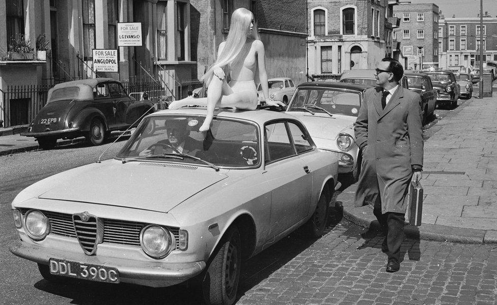 A pedestrian's attention is caught by a fibreglass tailor's dummy, made by Gem's Ltd, sitting on top of a car in Lancaster Road, west London