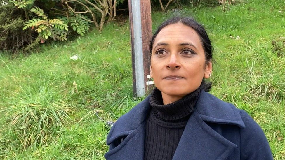 Meena Powell in a blue coat standing waiting for the bus