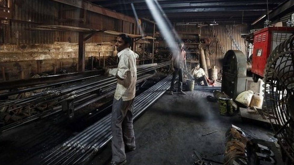 A worker carries an iron pipe inside a metal fabrication workshop in an industrial area of Mumbai