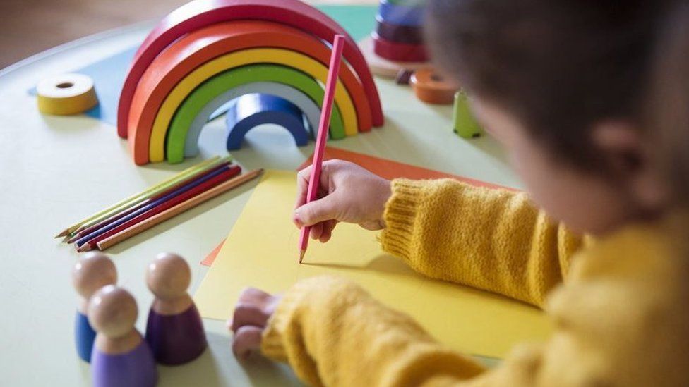 A child draws a picture while she is surrounded by toys