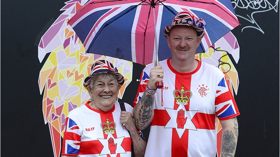 Man and woman wearing t-shirts with Ulster flags on them and union flag hats