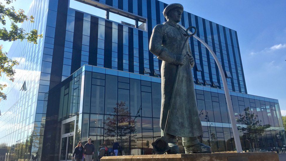 Corby Cube - modern steel and glass building with statue of steel worker in the foreground