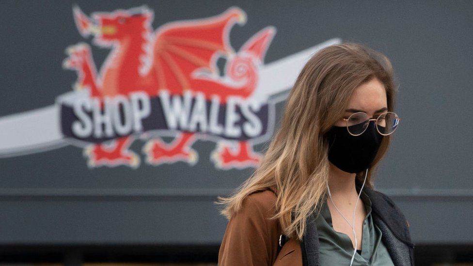 Woman wearing mask walks past 'Shop Wales' sign