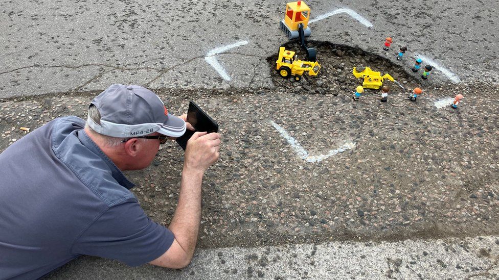 A man taking photograph of mini toys in pothole