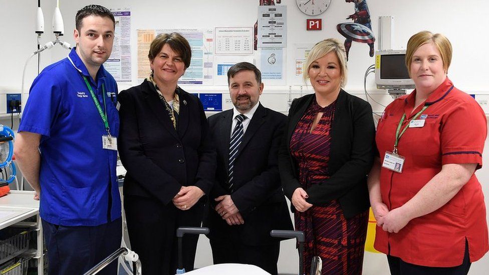Arlene Foster, Robin Swann and Michelle O'Neill pictured alongside health workers