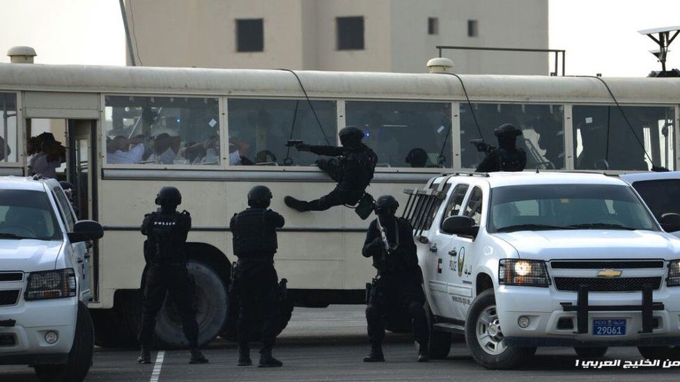 Security officer abseils across the front of a bus while other agents dressed in black point guns at the vehicle