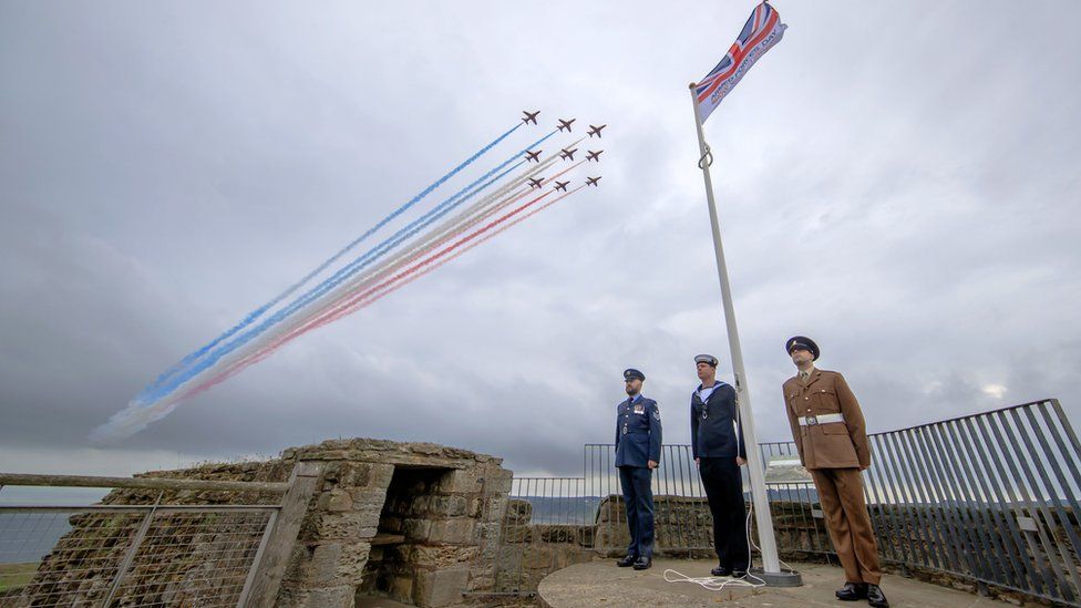 The Red Arrows pass over an Armed Forces Day flag in the castle grounds