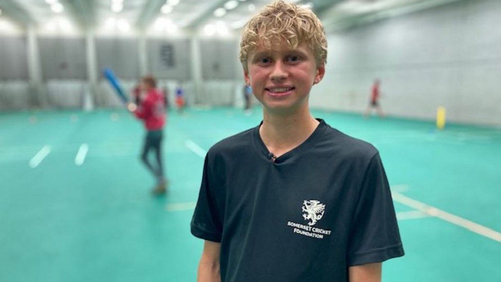 Matthew stands smiling at an indoor cricket court