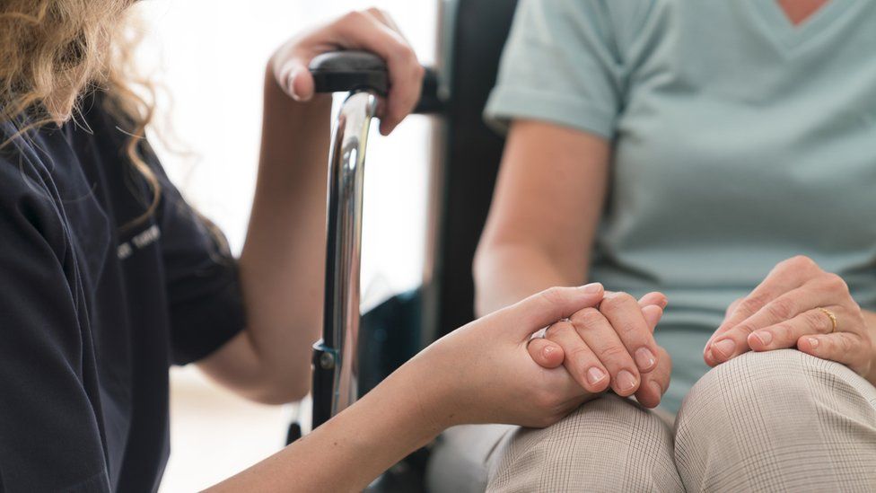Carer holding hand of disabled woman