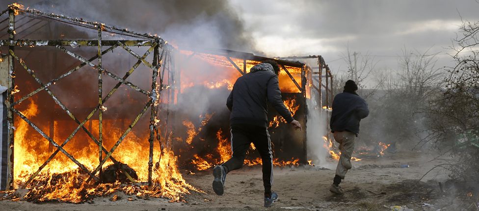 Migrants run past burning tents in the "Jungle" camp