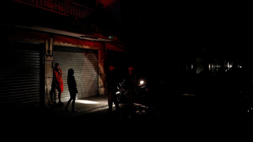 People use the light of a motorcycle to illuminate them as they talk on the street during a blackout in Caracas