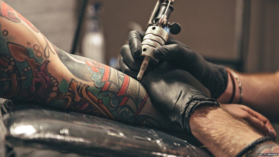 Tattooist creating a design on the arm of a man